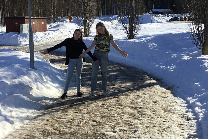 Solen skiner och två elever som står bland snöhögarna utan jackor.